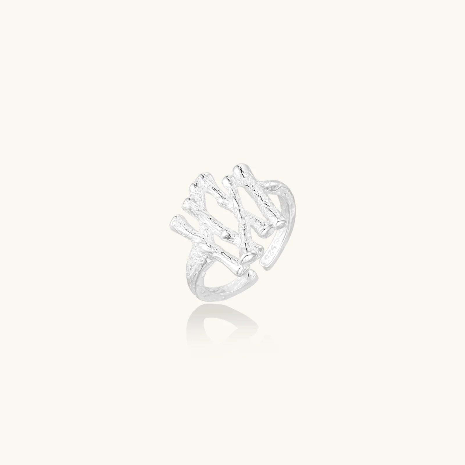 Sculptural sterling silver ring with organic branch design and textured surfaces on cream background