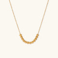 Delicate gold-plated necklace with graduated spherical beads forming gentle smile curve on beige background