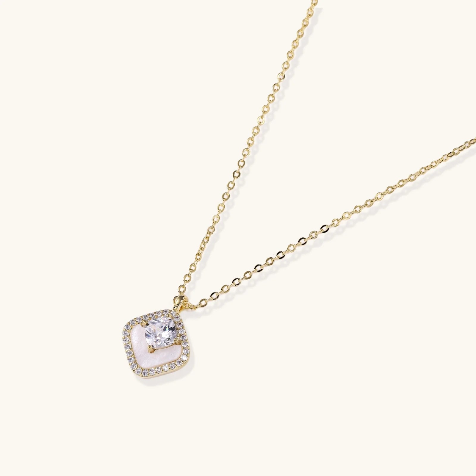 Gold quatrefoil pendant with crystal center on iridescent mother-of-pearl base, adjustable gold chain on cream background